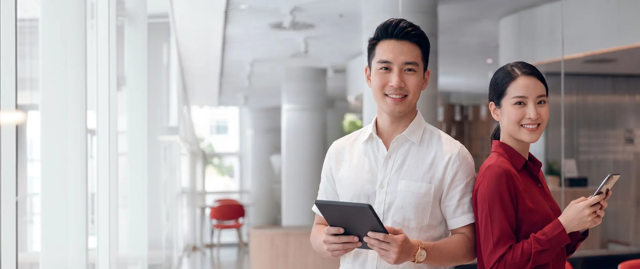 A man in a maroon blazer smiling at his phone in a bright office lobby