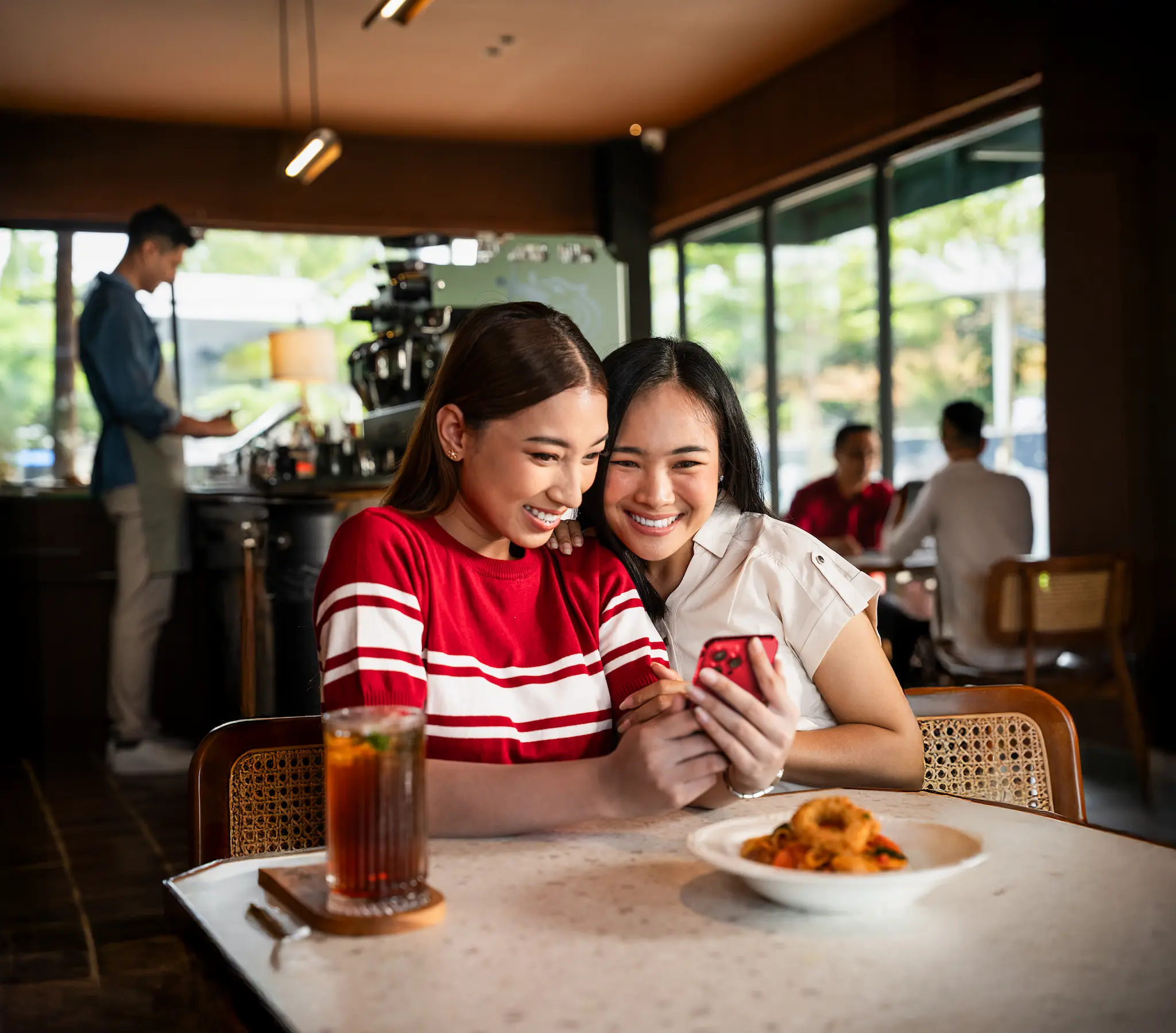 Two friends smiling at a phone together in a cafe, looking at the Privy app